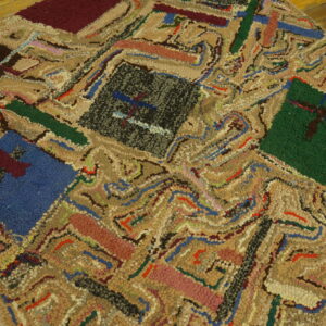 Highly textured patchwork rug featuring beige loops and blocks of blue, black, green, and maroon on wood planks.