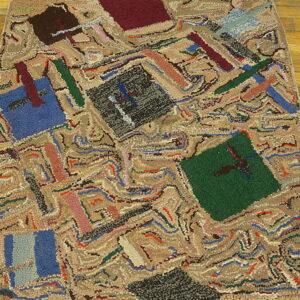 Highly textured abstract rug with blue, red, and green geometric blocks resting on warm wooden floor planks.