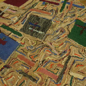 Close-up of a hooked texture rug with colorful geometric blocks and tan swirling patterns on wood flooring.