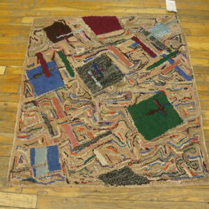 Abstract hooked rug with multicolored geometric patterns on distressed honey-toned wood plank flooring.