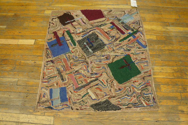 Abstract hooked rug with multicolored geometric patterns on distressed honey-toned wood plank flooring.