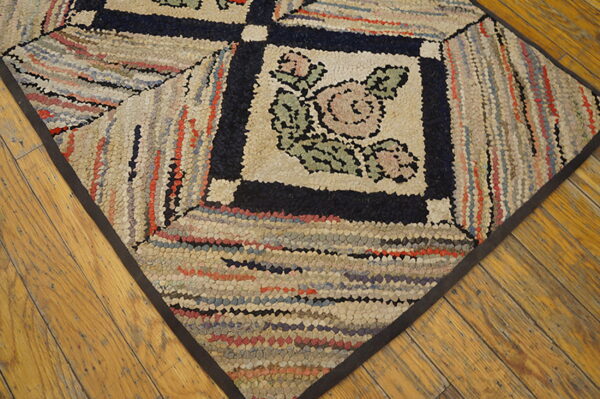 Multicolored hooked rug featuring a central rose motif and dark geometric borders on distressed hardwood floors.