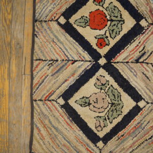 Hooked rug with multicolored diagonal stripes and navy floral diamonds on distressed wood flooring.