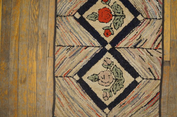 Hooked rug with multicolored diagonal stripes and navy floral diamonds on distressed wood flooring.