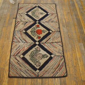 Multicolored hooked runner rug featuring three diamond panels with floral motifs rests on worn wood flooring.
