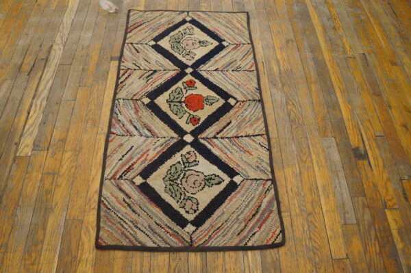 Multicolored hooked runner rug featuring three diamond panels with floral motifs rests on worn wood flooring.