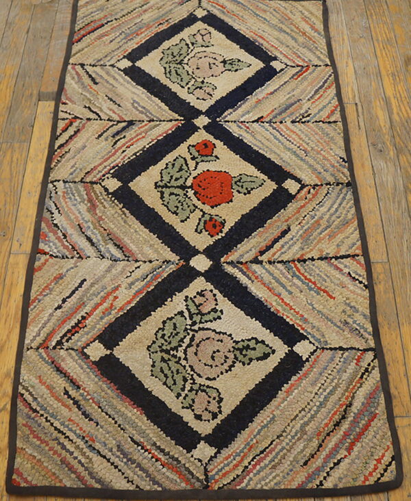 Textured runner with navy diamond trellis containing pink and red floral designs, laid on wide wooden floorboards.