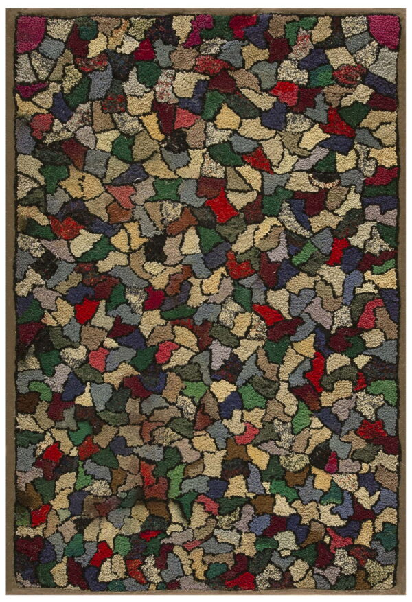A hooked rug displays an irregular mosaic pattern in shades of red, green, beige, and blue with a brown border.