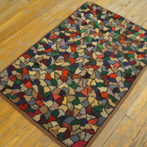 A textured, small rug with a multi-colored abstract patchwork pattern rests on wide plank wood flooring.