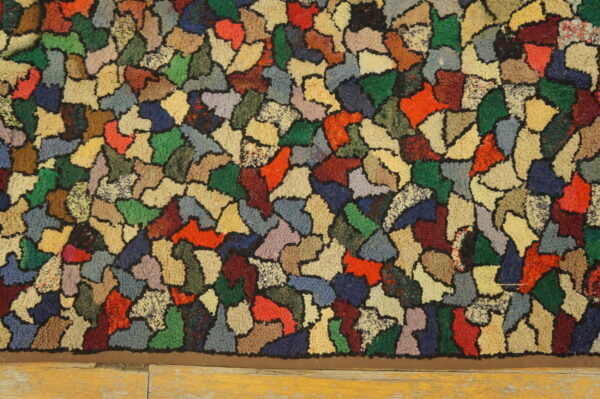 A multicolored, chunky rug features irregular color blocks outlined in black resting on light wood flooring.