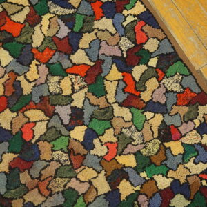 A brightly multicolored rug with irregular patch shapes rests on worn yellow wood flooring.