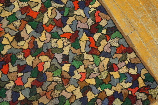A brightly multicolored rug with irregular patch shapes rests on worn yellow wood flooring.