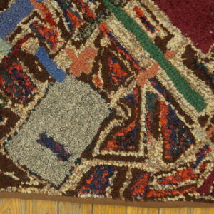 A high-pile rug with geometric patterns in brown, cream, gray, blue, and red rests on wood planks.