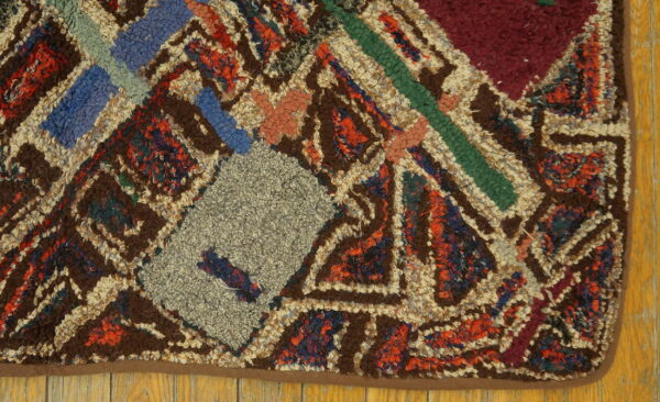 A high-pile rug with geometric patterns in brown, cream, gray, blue, and red rests on wood planks.