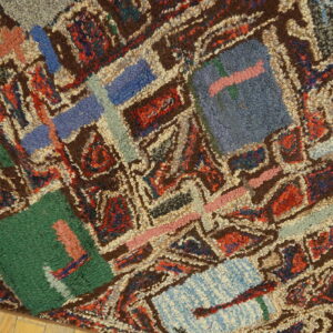 Close view of a shaggy, colorful rug with brown, blue, red, and green geometric patterning on wood.