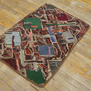 Textured rug with abstract blocks of red, blue, green, and brown geometric patterns rests on distressed wood planks.