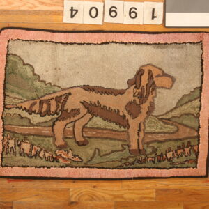 Low-pile rug depicting a brown dog in a green landscape with a pink textured border on hardwood.