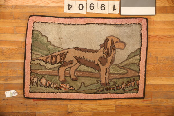 Low-pile rug depicting a brown dog in a green landscape with a pink textured border on hardwood.