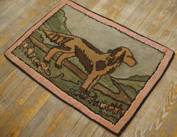Hooked rug with a tan dog jumping across a green landscape, featuring a dusty pink border on wood floors.