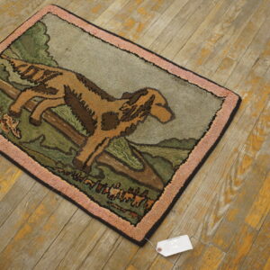 Small area rug with a tan and brown dog pattern, green fields, and pink border, on distressed wood floor.
