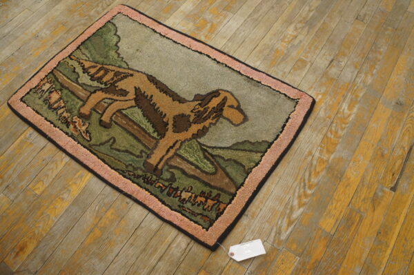 Small area rug with a tan and brown dog pattern, green fields, and pink border, on distressed wood floor.