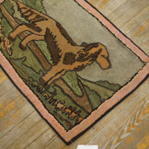 Tan and green scenic rug depicting a leaping animal, framed by a thick pink border on rustic wood flooring.
