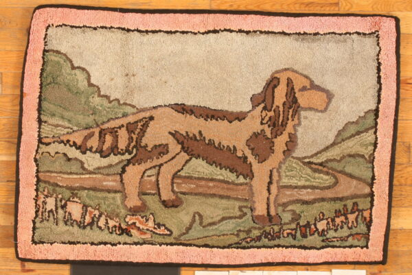 Pictorial hooked rug featuring a brown dog standing in a green and tan landscape with a textured pink border.