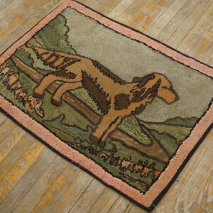 Brown and green pictorial rug with a hooked texture and pink border sits on weathered hardwood planks.