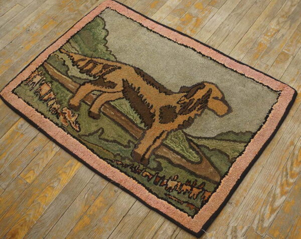 Brown and green pictorial rug with a hooked texture and pink border sits on weathered hardwood planks.