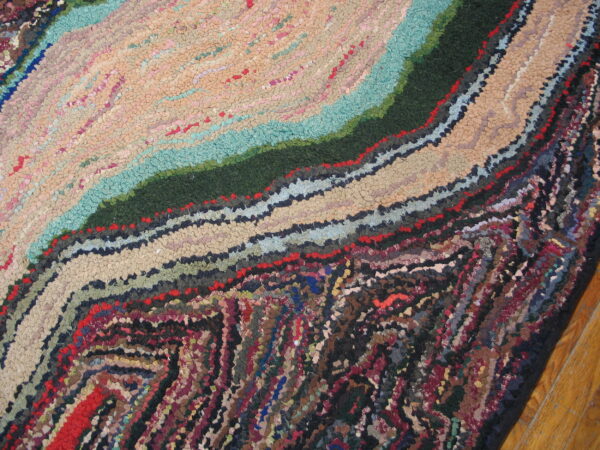 Textured rug detail with swirling bands of beige, teal, dark green, and mixed colors on a wood floor.