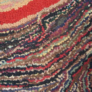 Abstract close-up of a textured rug with bands of red, tan, and densely packed multicolored fabric scraps forming curved patterns.