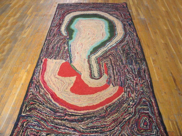 Abstract rug with cream, red, green, and teal shapes bordered by thick, dark, textured swirls on hardwood.