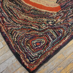 Chunky, high-textured multicolored rug with swirling stripes and an orange center on light wood planks.