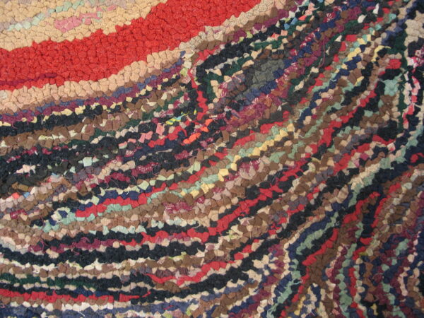 Hooked rug texture detail showing a broad red band beside variegated strips of brown, black, blue, and green.