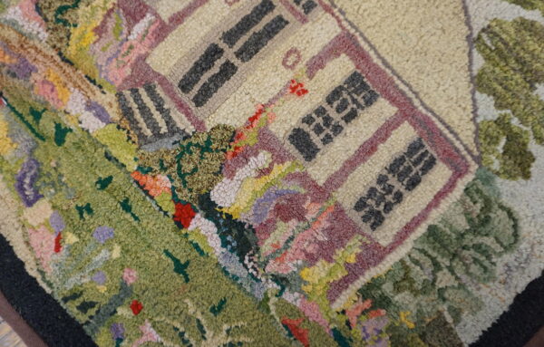 Textured rug with a detailed multicolored pictorial design showing a beige house and green landscape.