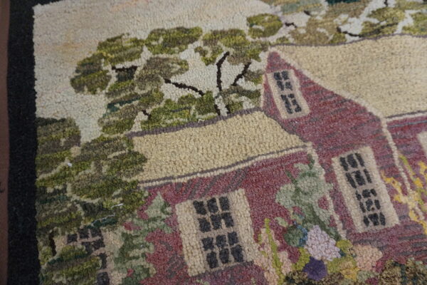 Detail of a looped rug featuring a pictorial motif of a reddish house surrounded by olive green foliage.