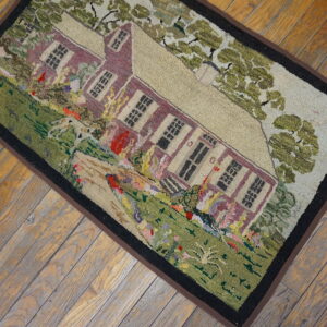 Rustic multi-colored rug with high-relief house and landscape pattern rests on distressed wood flooring.