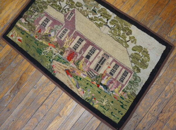 Rustic multi-colored rug with high-relief house and landscape pattern rests on distressed wood flooring.