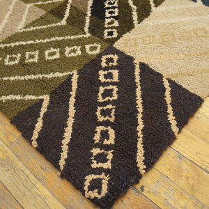 Textured, geometric rug in beige, green, and dark brown blocks rests on distressed plank flooring.
