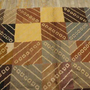 Geometric patchwork rug in various browns, yellow, and gray with a visible looped texture on wood floor.