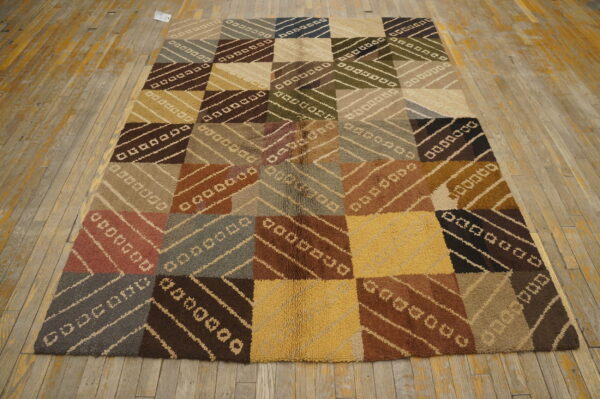 Earth-toned high-pile rug displays a large checkerboard of squares filled with diagonal stripe patterns on distressed wood flooring.
