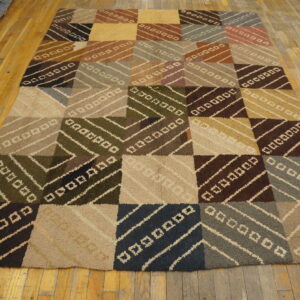 Earthy colored patchwork rug featuring textured squares with diagonal stripes rests on worn wood plank flooring.