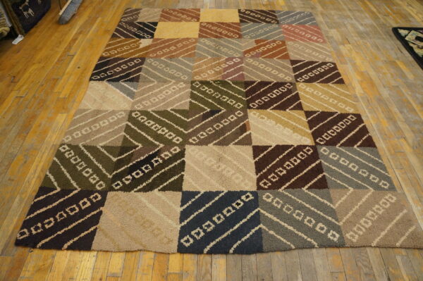 Earthy colored patchwork rug featuring textured squares with diagonal stripes rests on worn wood plank flooring.