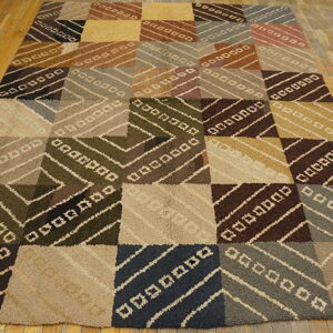 Multi-color, low-pile rug with a large geometric block pattern rests on distressed hardwood flooring.
