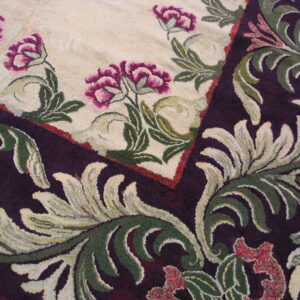 Textured detail of a rug corner showing magenta flowers on cream bordered by dark purple scrollwork.
