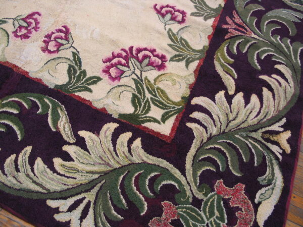 Textured detail of a rug corner showing magenta flowers on cream bordered by dark purple scrollwork.