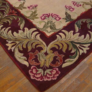Burgundy border and green scrolling foliage frame a cream field with pink flowers on hardwood flooring.