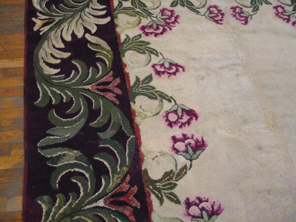 Textured rug detail showing a dark plum border with green leaves next to a cream field with pink flowers on wood flooring.