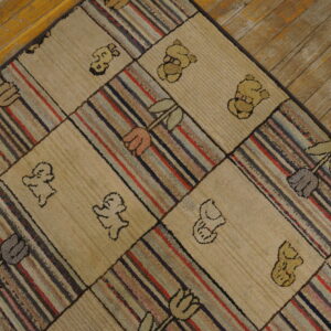 Patchwork hooked rug with striped, floral, and bear squares lying on distressed wood floorboards.