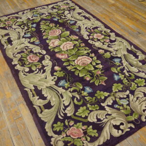 Dark purple rug with sculpted pink rose and sage green scroll patterns on a distressed wood floor.